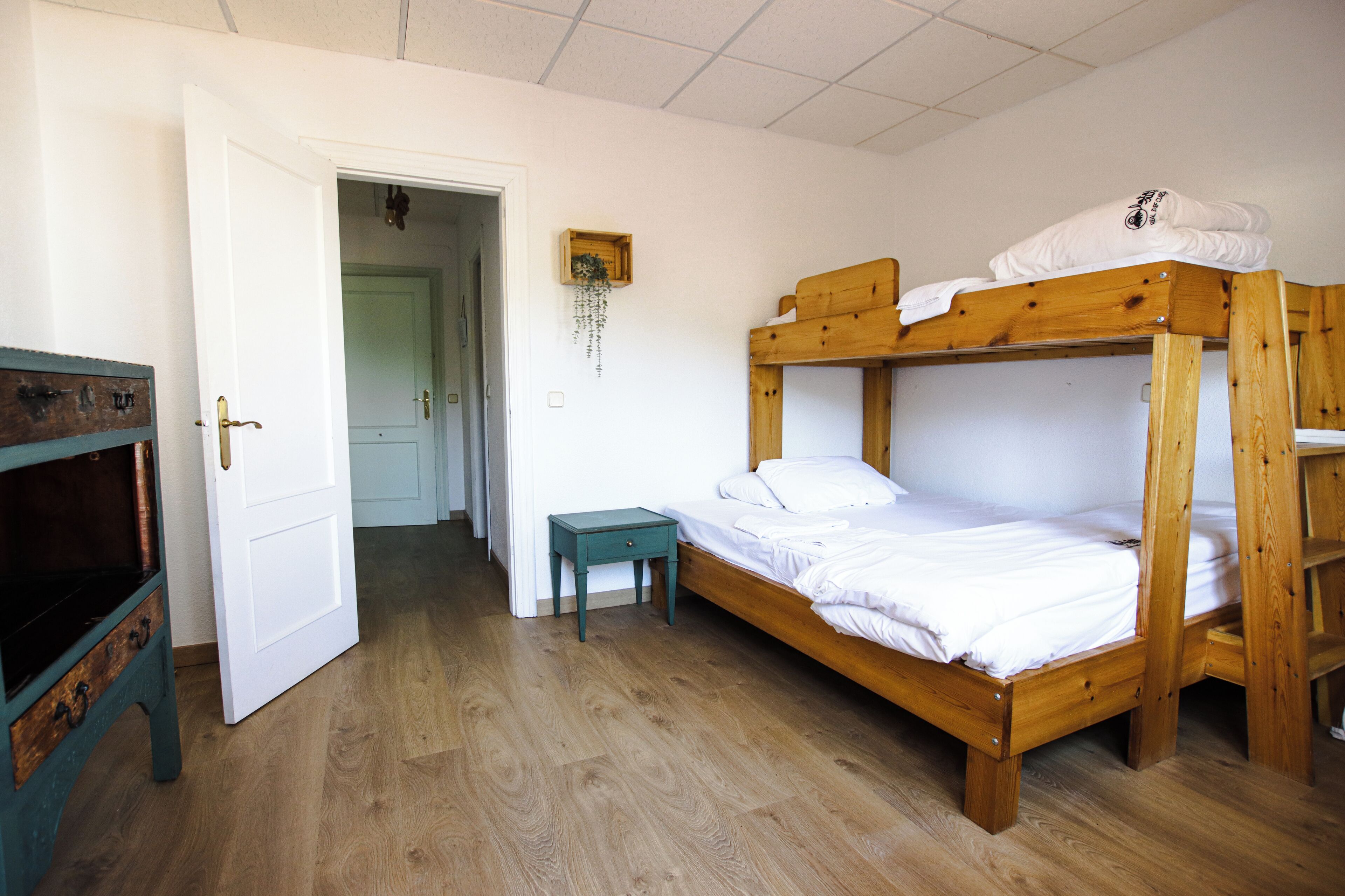 Una habitación con literas, una mesita pequeña y una puerta que da a otra habitación.