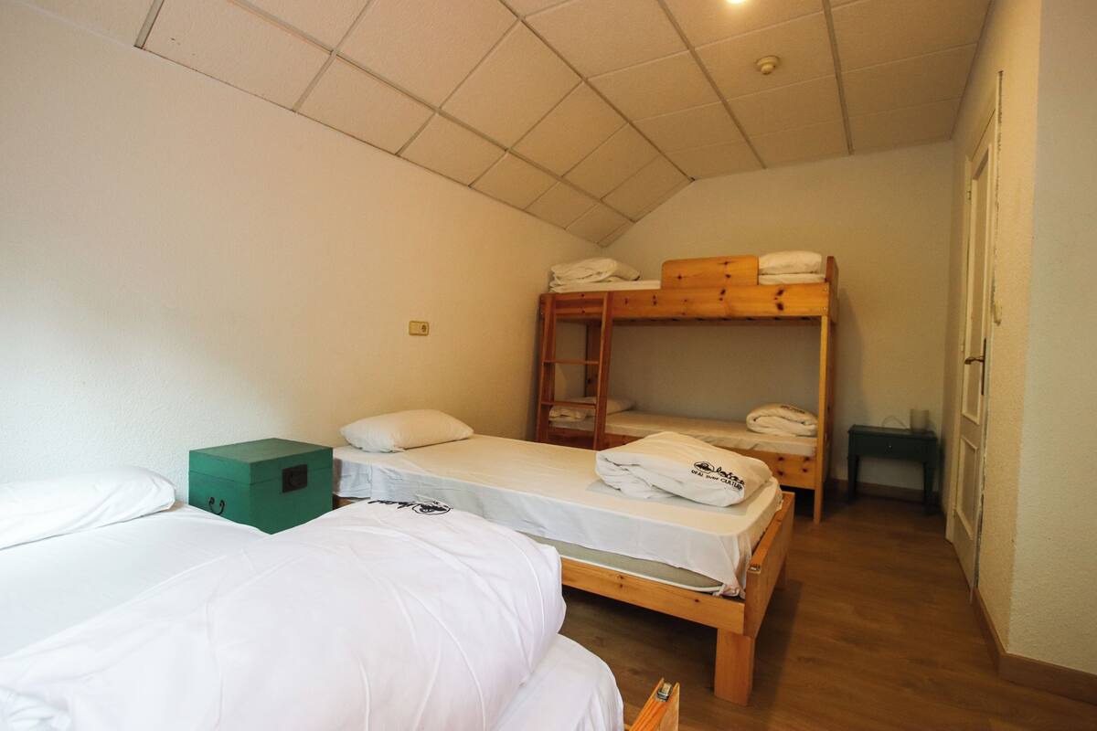 A dormitory room with bunk beds, a green storage box, and a wooden desk.