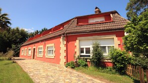 A red house with a tiled roof, a stone pathway leading to the entrance, and a wooden fence. - Arena Surf Hotel (Somo)