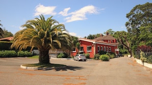 A red house with a car parked in front, surrounded by greenery and a clear sky. - Arena Surf Hotel (Somo)