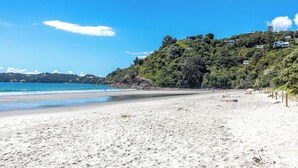 A beach with a clear sky, sandy shore, and a hill with buildings.