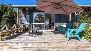 A wooden deck with a table and chairs, a large umbrella, and a sign reading 'The Beach House.'