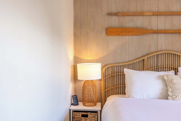 Une chambre à coucher bien rangée, avec une tête de lit en bois, une lampe de chevet et un couvre-lit blanc.