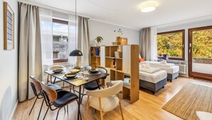 Una sala de estar moderna con comedor, un sofá, una estantería y vistas a árboles otoñales.
