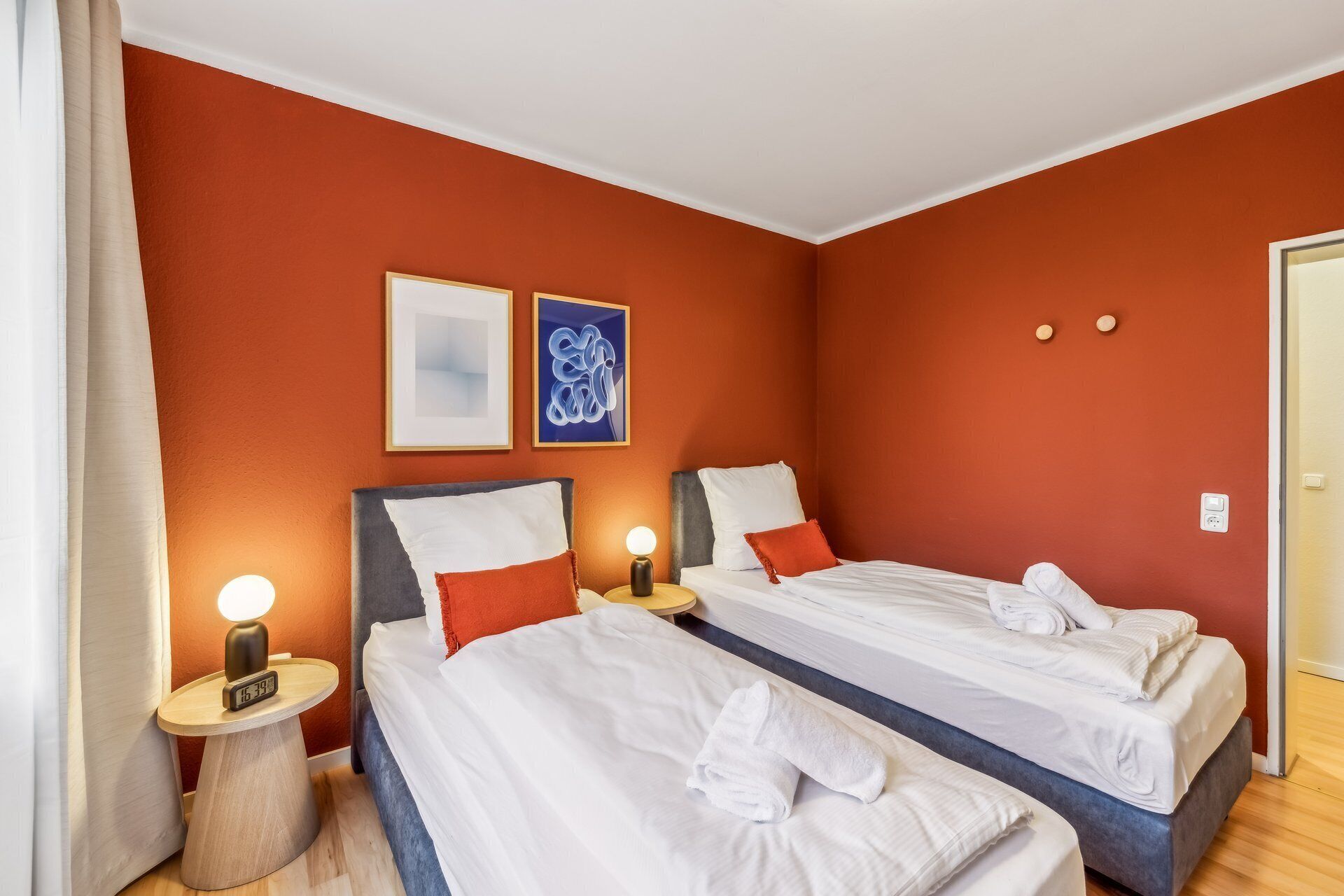 Habitación de hotel con dos camas, una mesita de noche con lámpara y dos cuadros enmarcados en la pared.