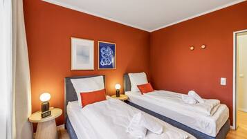Habitación de hotel con dos camas, una mesita de noche con lámpara y dos cuadros enmarcados en la pared.