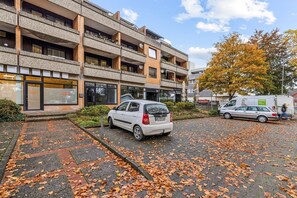 Un edificio de varios pisos con un estacionamiento cubierto de hojas caídas.