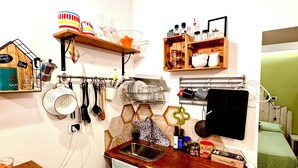 Una cocina compacta con encimera de madera, un fregadero y un refrigerador pequeño. Hay estantes sobre la encimera con diversos utensilios de cocina y una pequeña ventana sobre el fregadero.