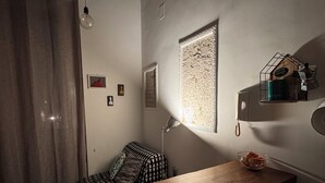 Una habitación acogedora con una mesa de madera, un sofá estampado, un ventanal con papel decorativo y un estante de pared con una vela.
