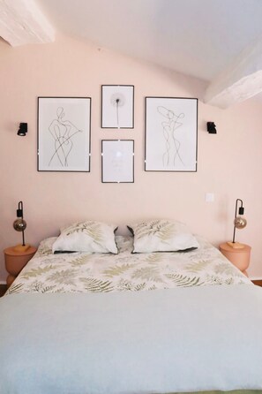 Une chambre à coucher comprenant un lit, deux lampes fixées au mur et trois œuvres d’art encadrées.