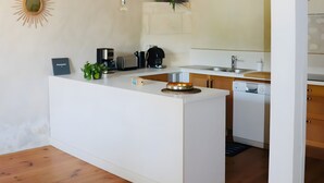Een moderne keuken met een centraal eiland, houten vloeren, hanglampen en een zonachtige decoratie aan de muur.