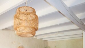 Een eetruimte met een tafel gedekt voor vier personen, witte stoelen, een geweven hanglamp, en een keuken op de achtergrond.