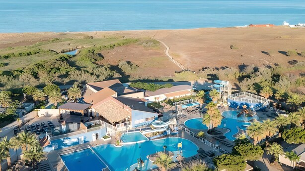 Eine Luftaufnahme eines Resorts mit mehreren Schwimmbecken, einem Strand und einer bergigen Kulisse.