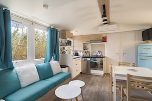 Een compacte keuken met moderne apparaten, een eethoek met een tafel en stoelen, en een bank met kussens in teal.