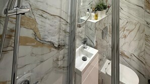 A modern bathroom with a glass-enclosed shower, marble walls, and a small sink with a mirror. - Farringdon Rooms (London)