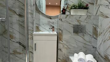 A bathroom with a glass shower enclosure, a white sink, a round mirror, a toilet, and a towel rack.
