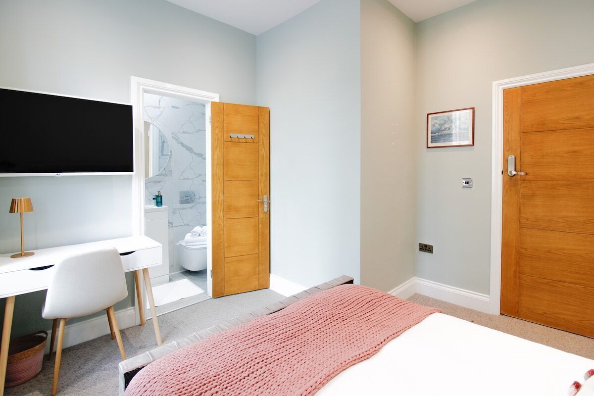 Une chambre à coucher comprenant un lit, un bureau, une chaise, un téléviseur et une porte donnant sur une salle de bain.