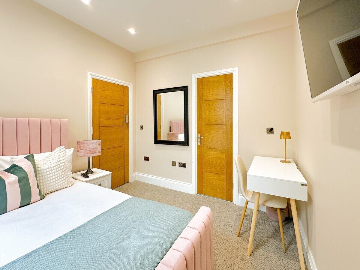 Une chambre à coucher comprenant un lit, une table de chevet, une lampe, un bureau, une chaise et un téléviseur fixé au mur.