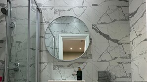 A bathroom with a glass-enclosed shower, a white cabinet, a round mirror, and a toilet with towels. - Farringdon Rooms (London)