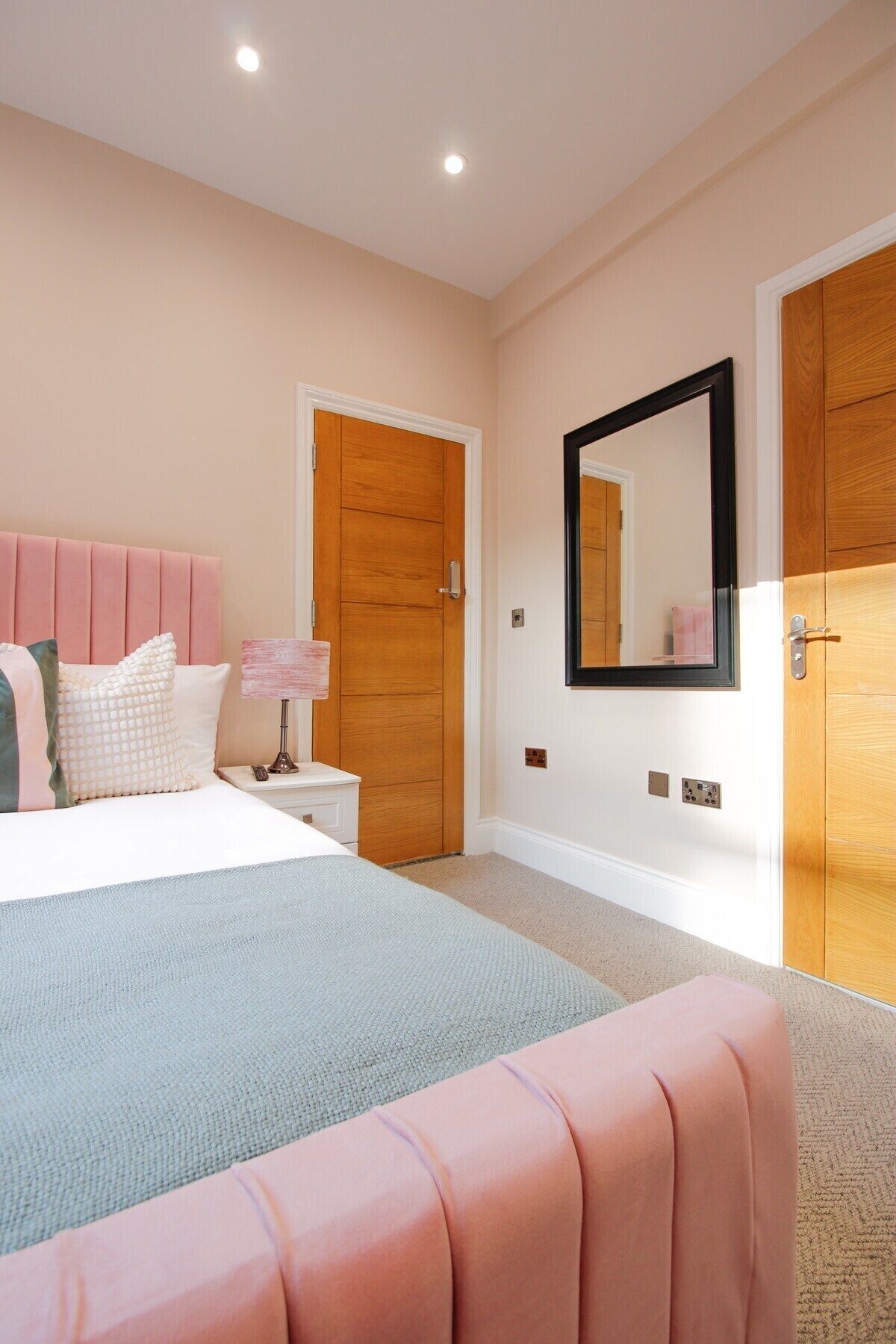 A bedroom with a bed, nightstand, dresser, and a mirror on the wall.
