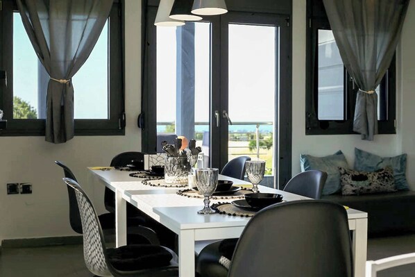 A dining area with a white table set for four, a sofa with cushions, and large windows with curtains.