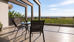 Un balcon avec une table et des chaises, un pot de fleurs et une vue sur un champ verdoyant et un paysage lointain.