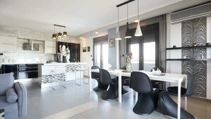 Une cuisine moderne avec des meubles blancs, des chaises noires et des luminaires suspendus.