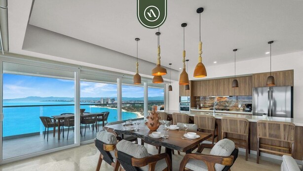 Une cuisine moderne avec vue sur l’océan, de grandes fenêtres et un coin repas comprenant une table et des chaises.