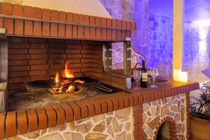 A brick outdoor grill with a stone base, a wine bottle, and glasses on a table.