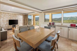 A spacious living area with a wooden dining table, comfortable seating, a flat-screen TV, and a stone accent wall.