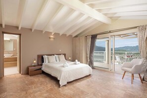 Une chambre dotée d’un grand lit, d’une table de chevet, d’une commode, d’une chaise, d’un balcon avec vue et d’une salle de bain avec un lavabo et un miroir.