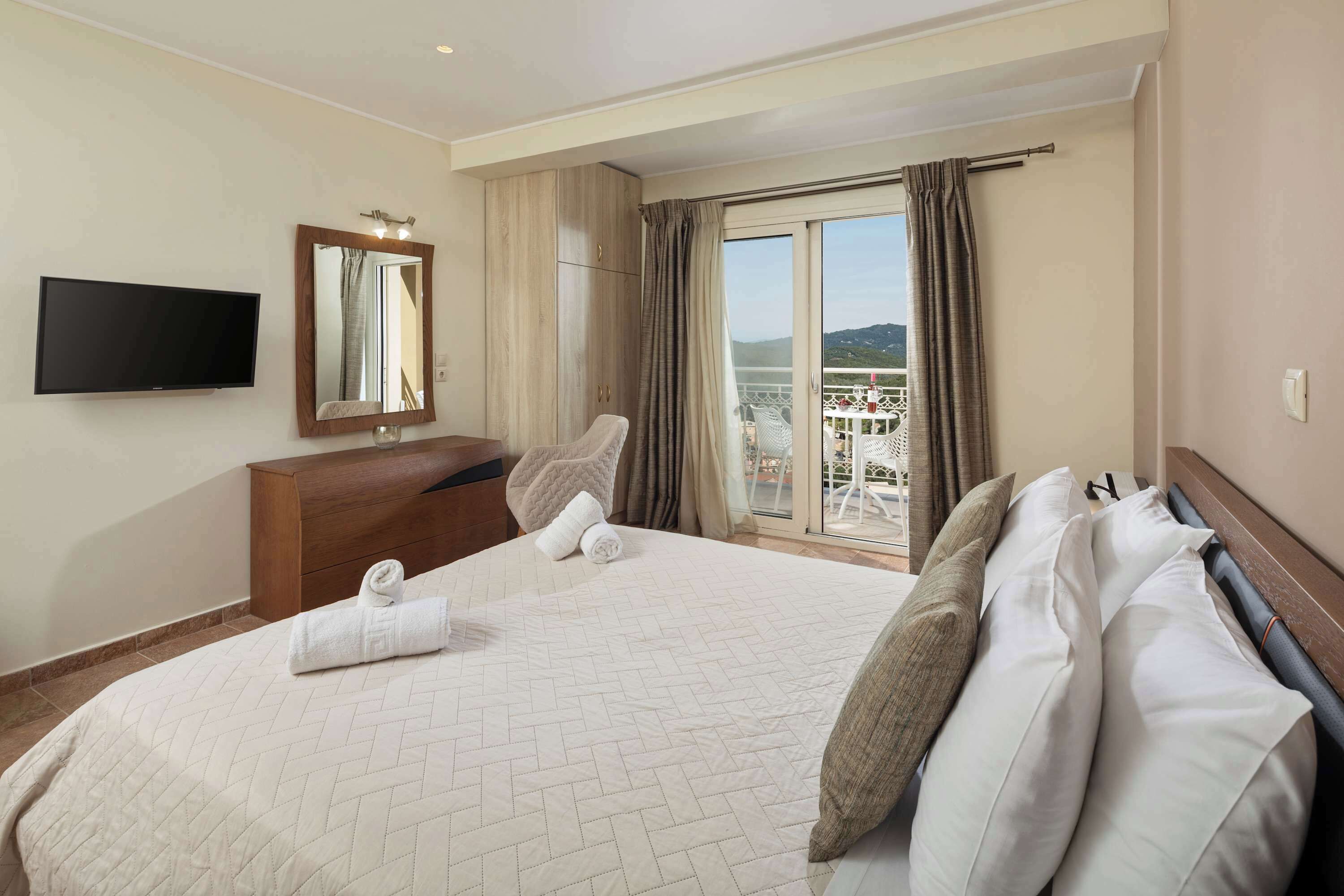 A hotel room with a large bed, a wooden dresser, a flat-screen TV, a mirror, and a balcony with a view.