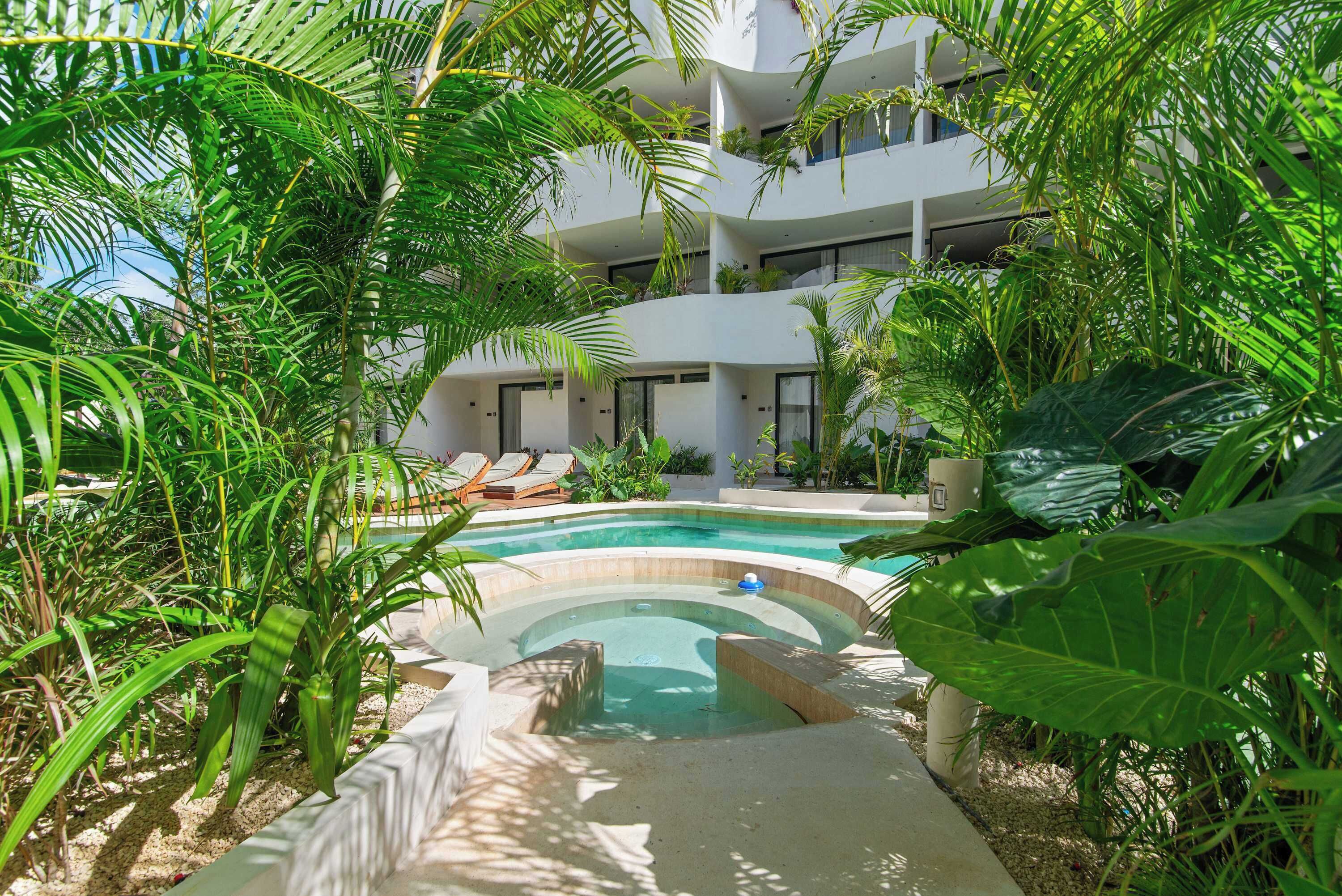 Un hotel moderno con piscina rodeada de exuberante vegetación, varios balcones y un jardín bien cuidado.