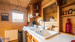 A wooden cabin kitchen with a large window, wooden cabinets, a sink, and a stove. - Chalet 'Jarrier' with Mountain View, Private Terrace and Private Garden (Jarrier)
