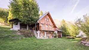 A wooden cabin with a stone foundation, a balcony, and a picnic table in a grassy area. - Chalet 'Jarrier' with Mountain View, Private Terrace and Private Garden (Jarrier)