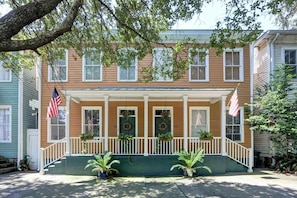 Ein zweistöckiges Haus mit Veranda, amerikanischen Flaggen und Topfpflanzen.
