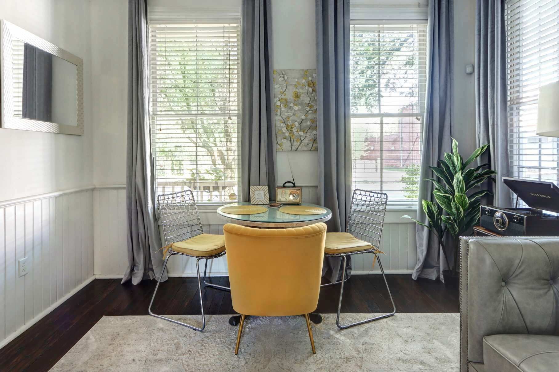A dining area with a round glass table, four yellow chairs, a radio, and a plant.
