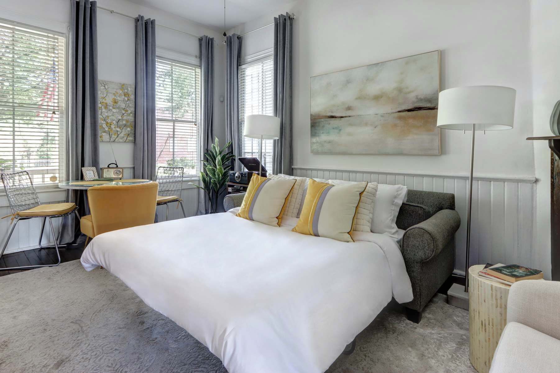 A hotel room with a large bed, a desk with a chair, a sofa, and a floor lamp.