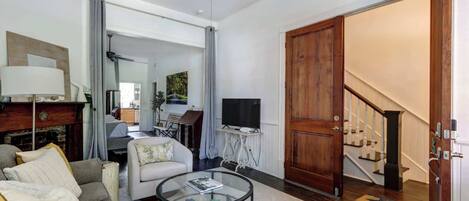 Una sala de estar con sofá, sillón, mesa de centro, televisor y una puerta de madera que da a una escalera.