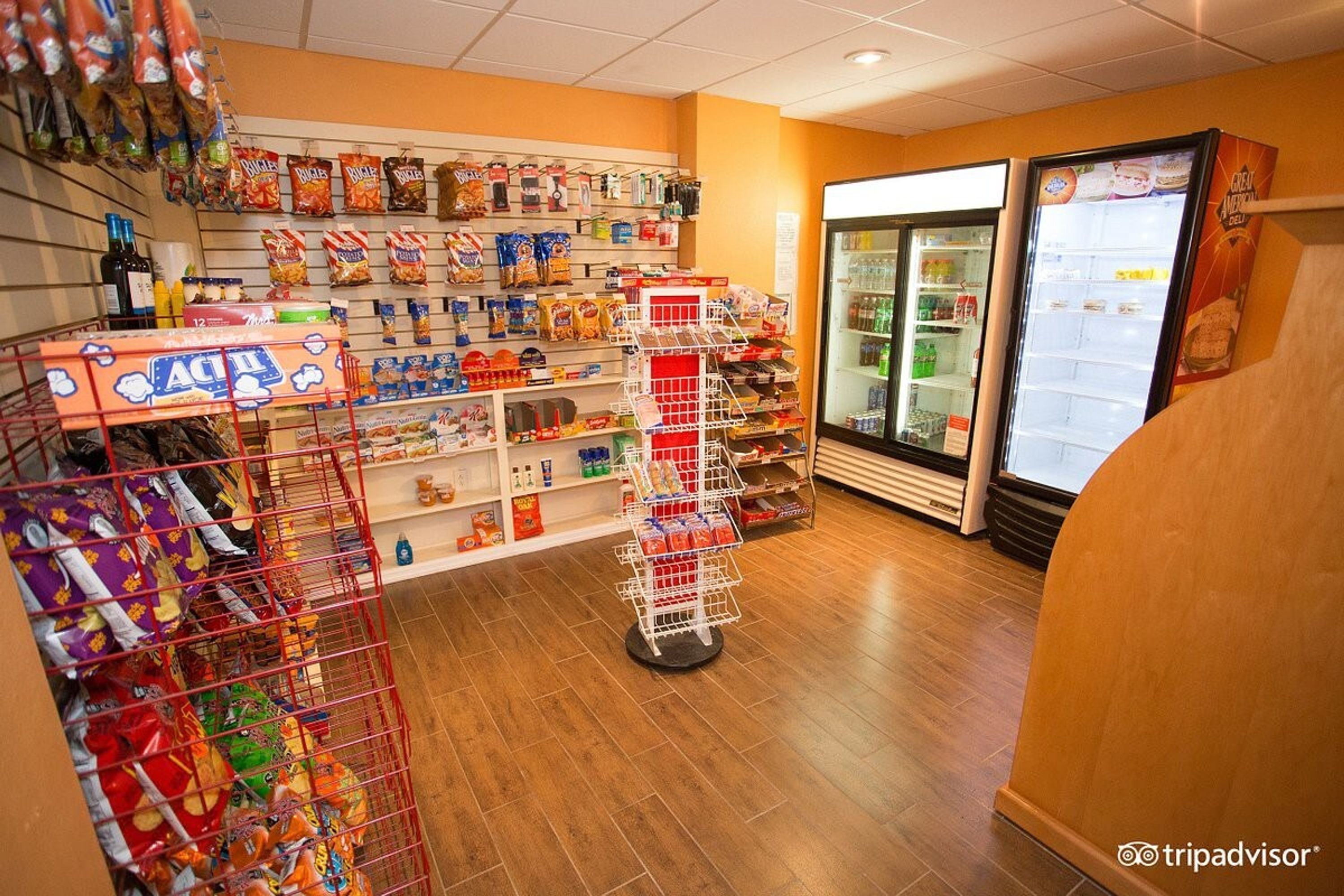 A grocery store interior with shelves stocked with snacks and beverages, a refrigerated display case, and a self-checkout area.