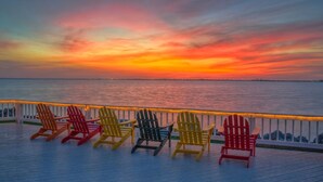 Una terraza con sillas Adirondack de colores que dan al atardecer sobre el agua.
