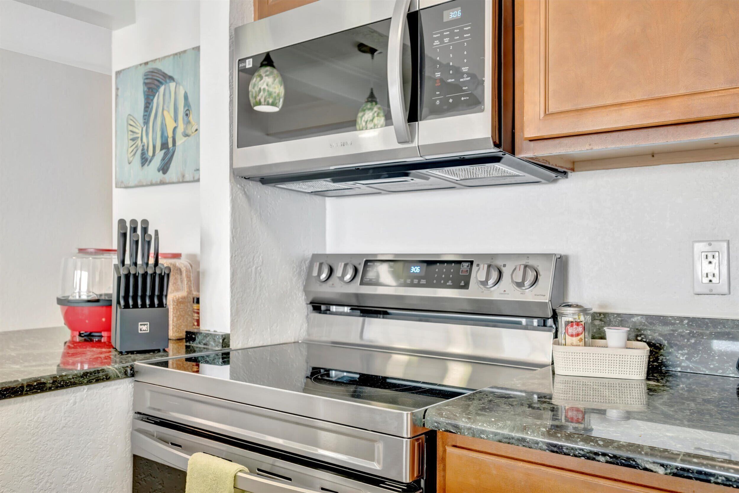 Cozinha com eletrodomésticos de aço inoxidável, micro-ondas, forno e um conjunto de facas sobre a bancada.