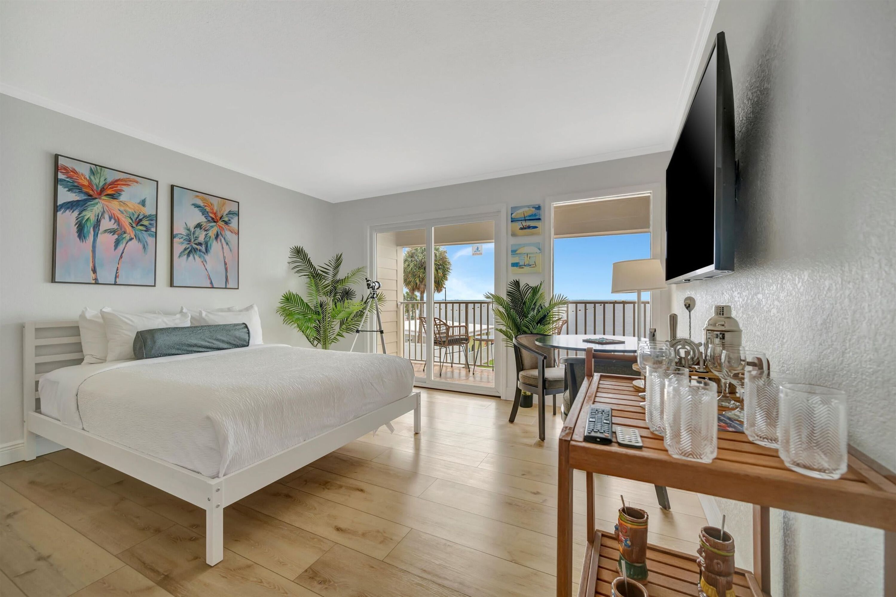 A bedroom with a bed, a balcony with a table and chairs, and a TV mounted on the wall.