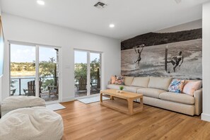 A modern living room with a beige sofa, a wooden coffee table, and a large window overlooking a balcony with outdoor furniture.