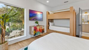 Ein modernes Schlafzimmer mit Etagenbett, einem farbenfrohen Schrank, einem großen Fenster mit Blick auf Grünflächen und einem Bild an der Wand.