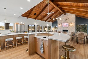 A spacious kitchen with a large island, wooden ceiling beams, and a stone fireplace. - Chasing Summer - Private Lakefront Luxury on Lake (Point Venture)