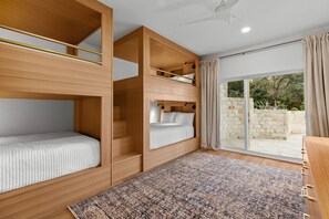 A room with a bunk bed, a desk, and a large window with a view of greenery.