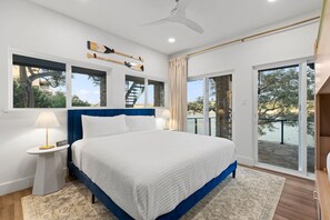 A bedroom with a large bed, a ceiling fan, and a view of a balcony with a railing.