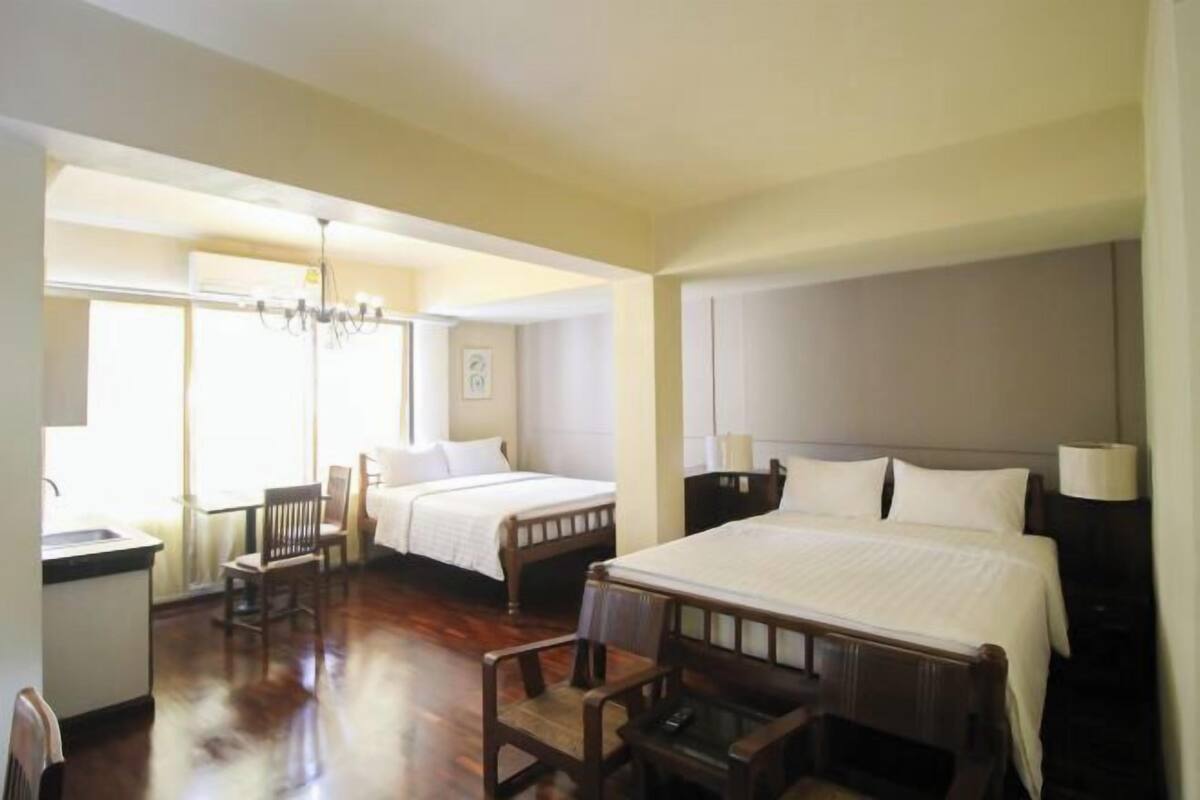 Une chambre d’hôtel avec deux lits, un bureau avec une chaise, un lustre et une vue sur l’extérieur par une porte ouverte.