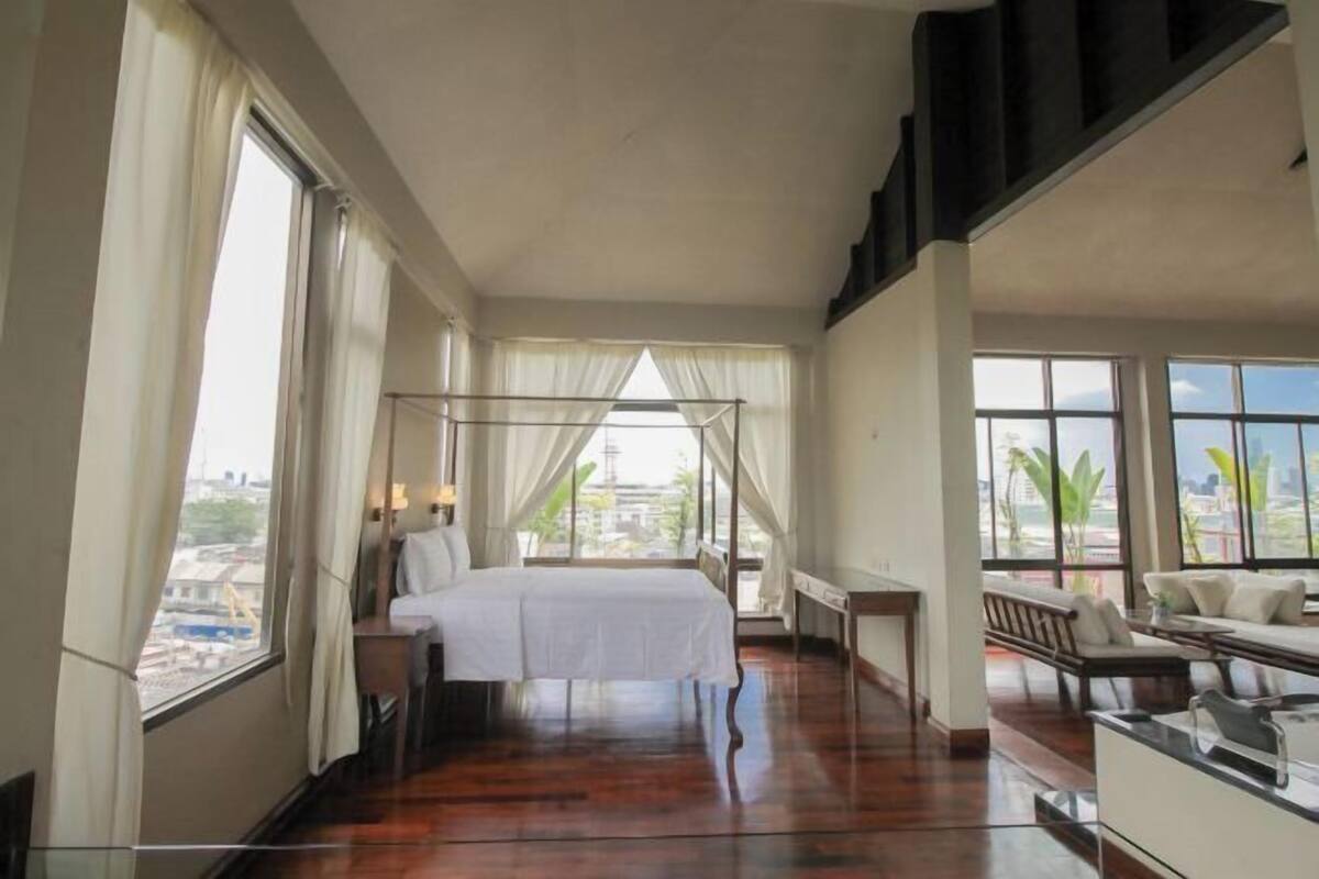Une chambre à coucher avec un lit à baldaquin, de grandes fenêtres, un balcon et une vue sur la ville.